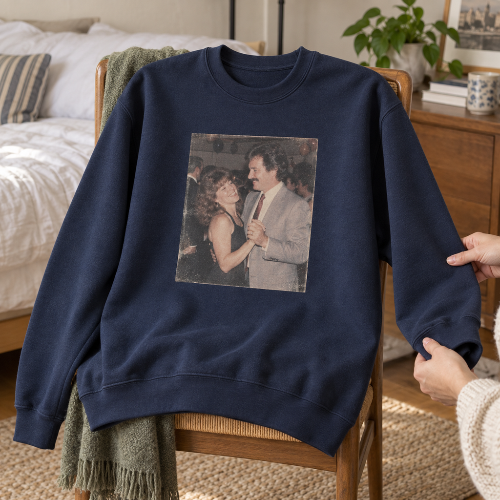 A navy personalized crewneck sweatshirt printed with an old photograph of a couple dancing, displayed on a bedroom chair.