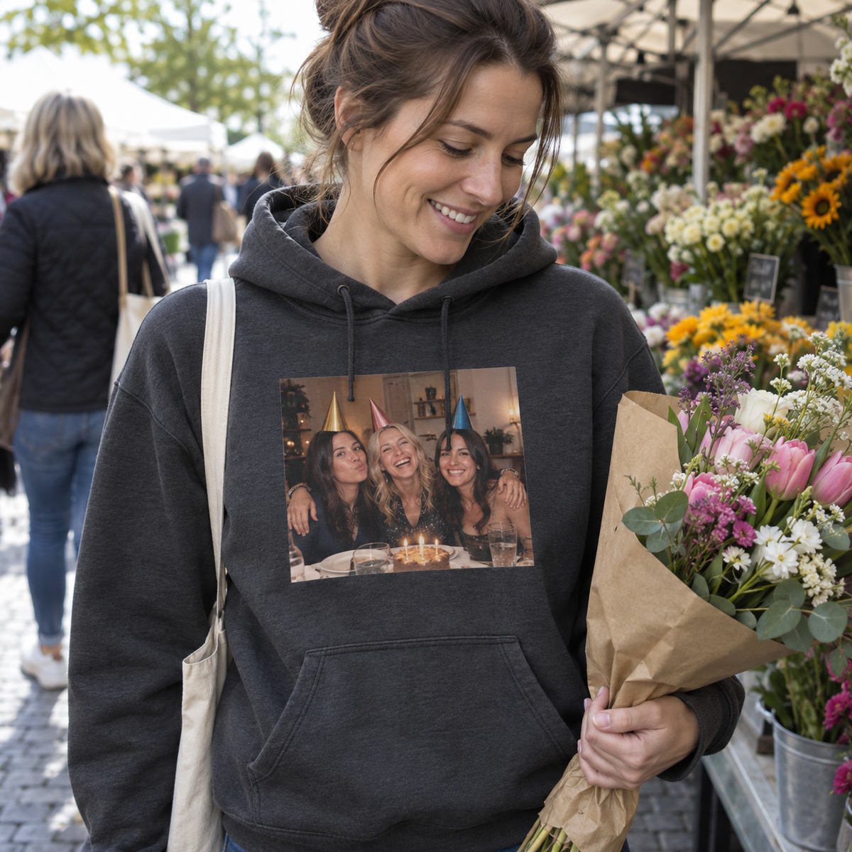 A charcoal photo hoodie printed with three friends in party hats, worn at a flower market.