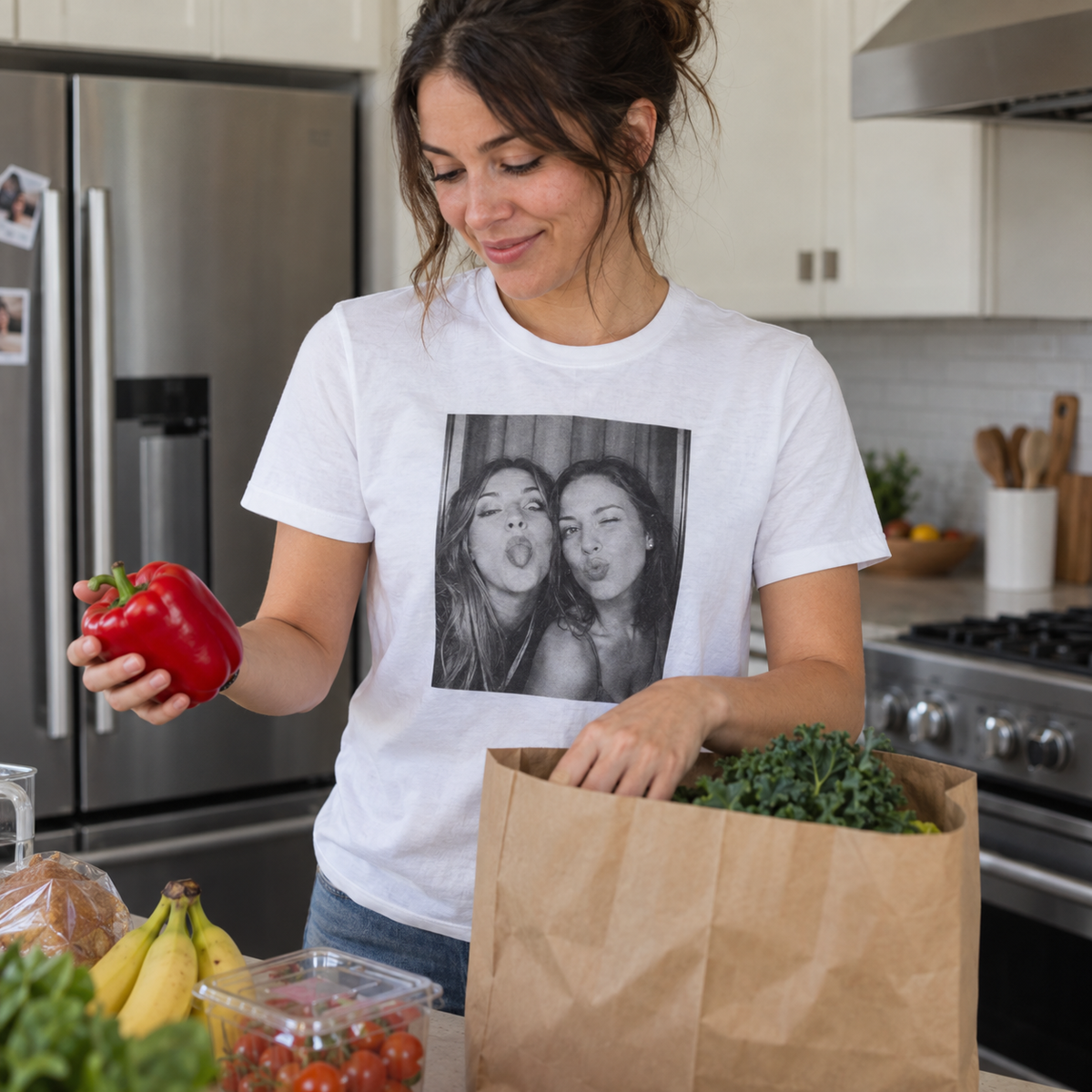A white personalized T-shirt printed with a funny photo booth portrait of friends, worn in a home kitchen.