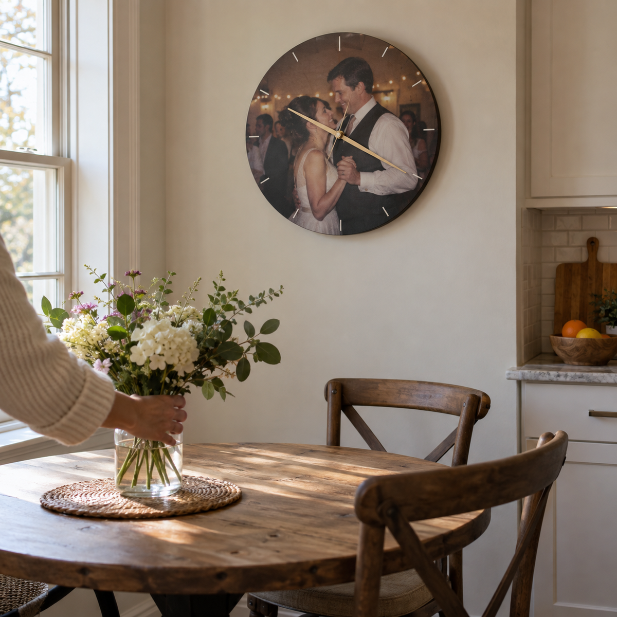 A round wall clock printed with a photograph of a couple dancing at a wedding, hanging above a kitchen table.