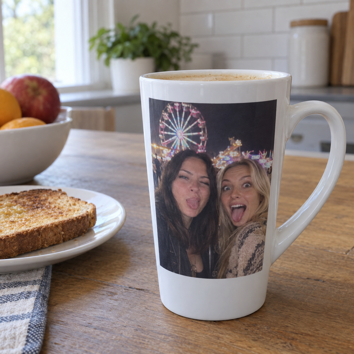 A tall tapered latte mug printed with a funny night carnival photo of two friends, on a sunny kitchen table.