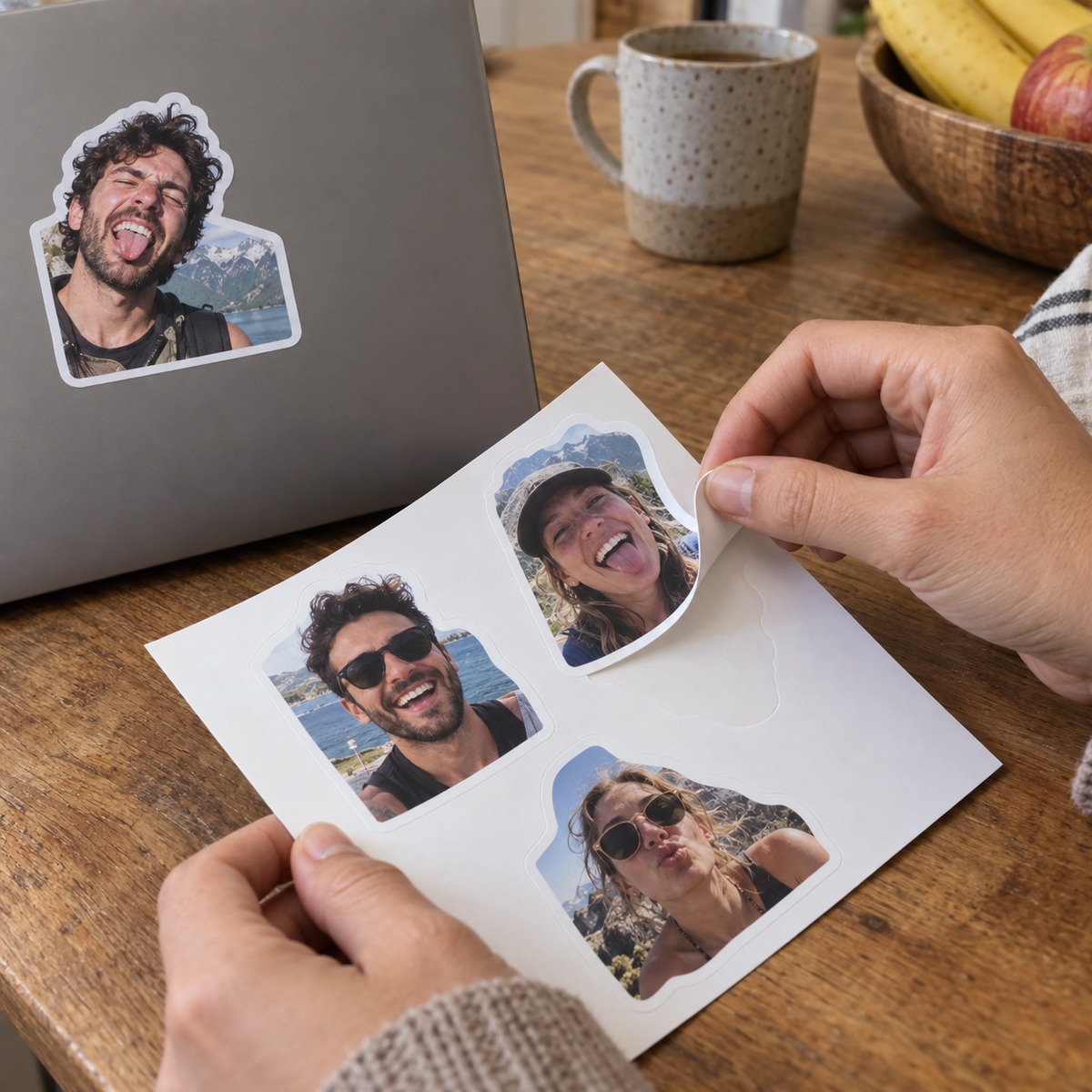 Personalized photo stickers with funny friends' portraits being peeled from a backing sheet beside a laptop.