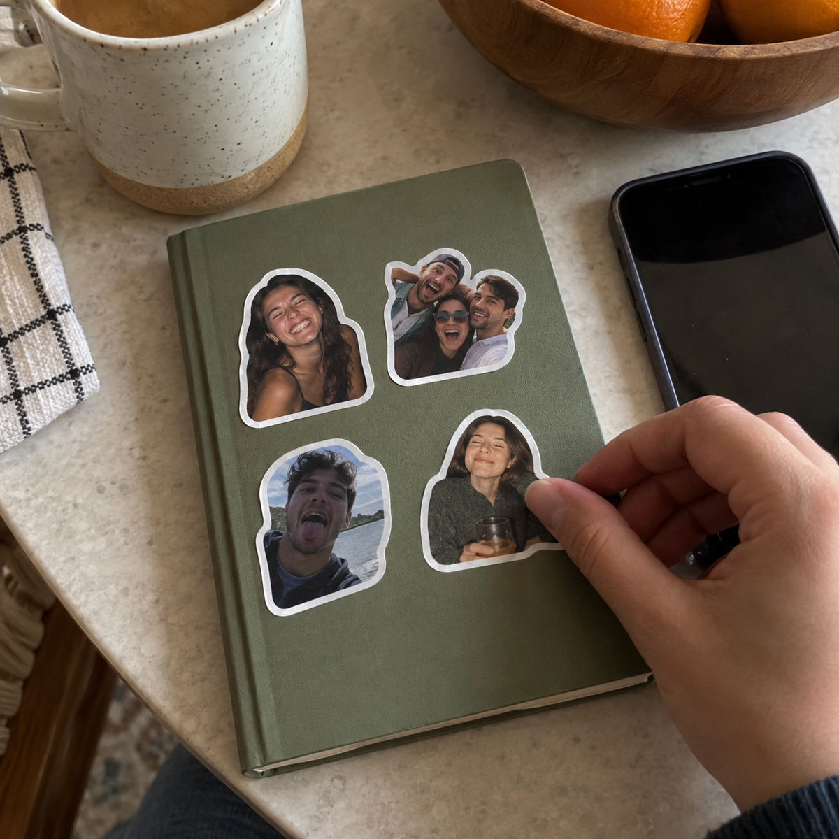 Four separate personalized portrait stickers with white borders being arranged on a plain notebook.