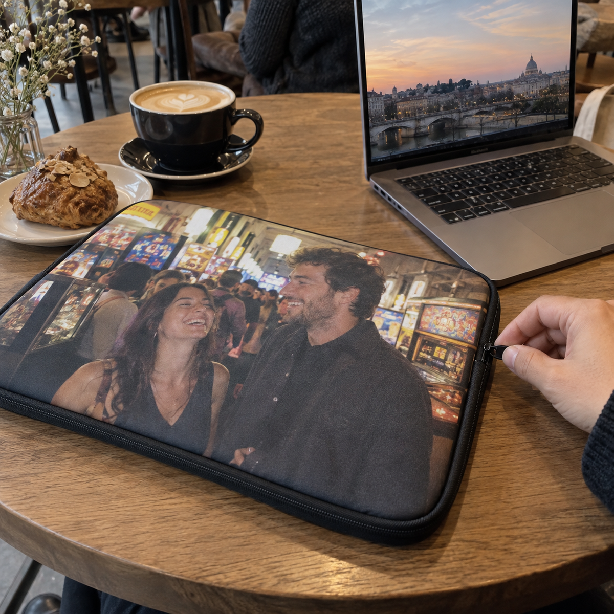 A laptop sleeve printed with a past photo of friends in an arcade on a café table.