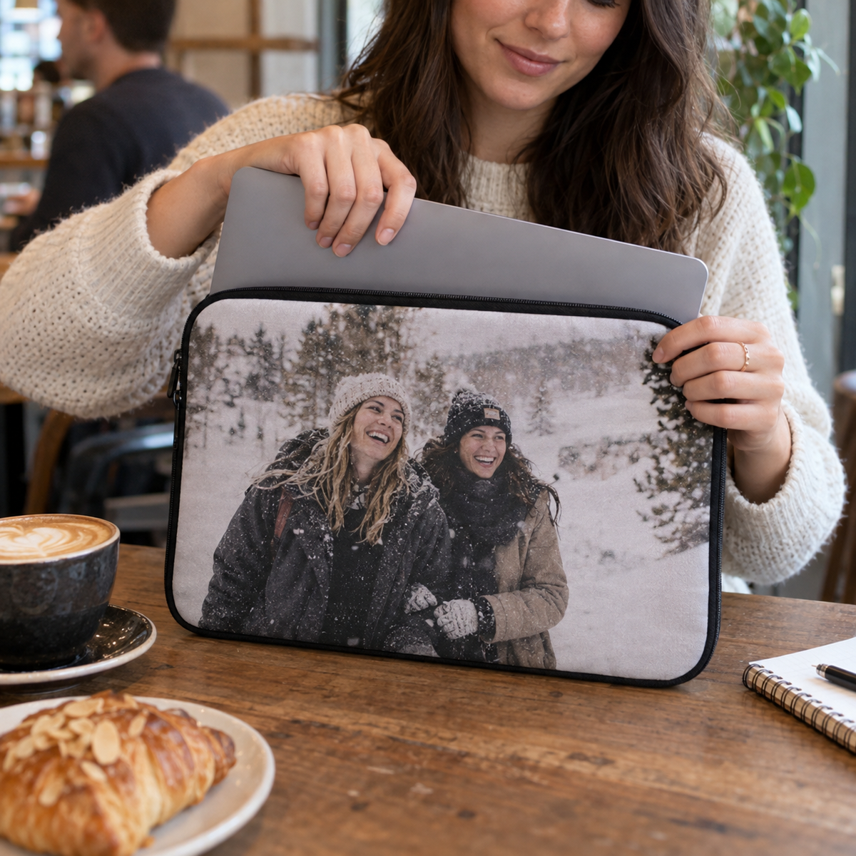 A padded laptop sleeve printed with a snowy friends' photo while a laptop is placed inside at a café.