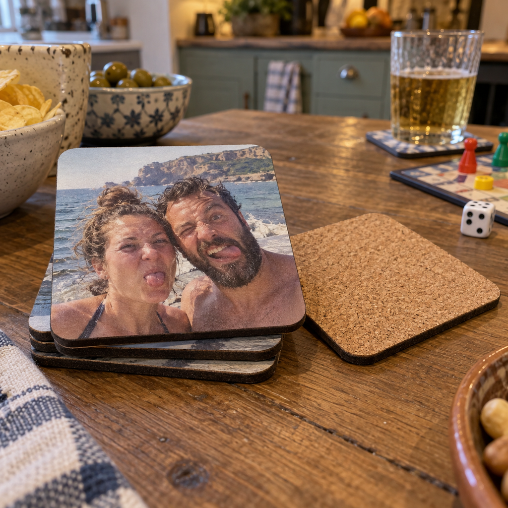 Personalized square cork-backed coasters printed with a funny seaside couple photo on a game-night table.
