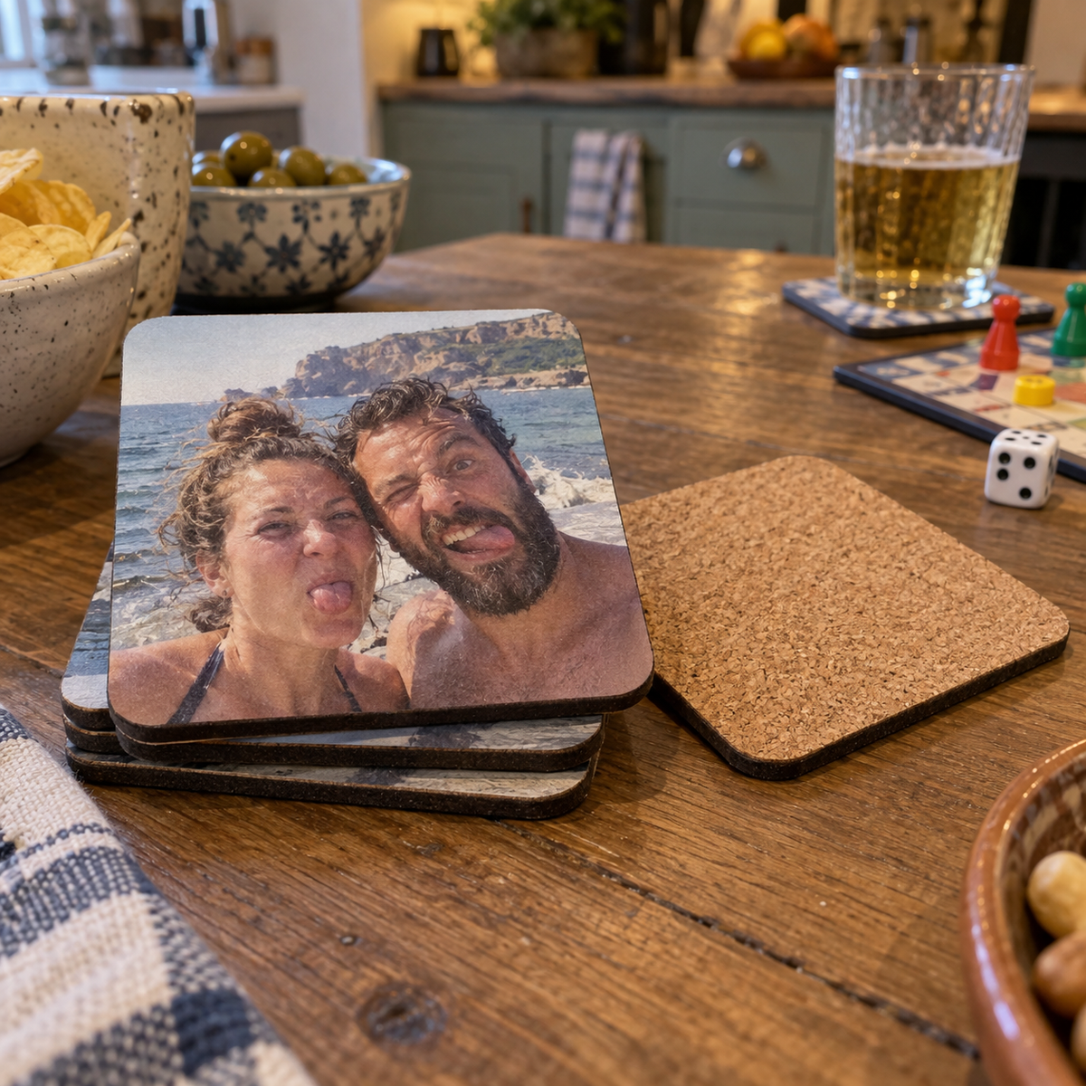 Personalized square cork-backed coasters printed with a funny seaside couple photo on a game-night table.