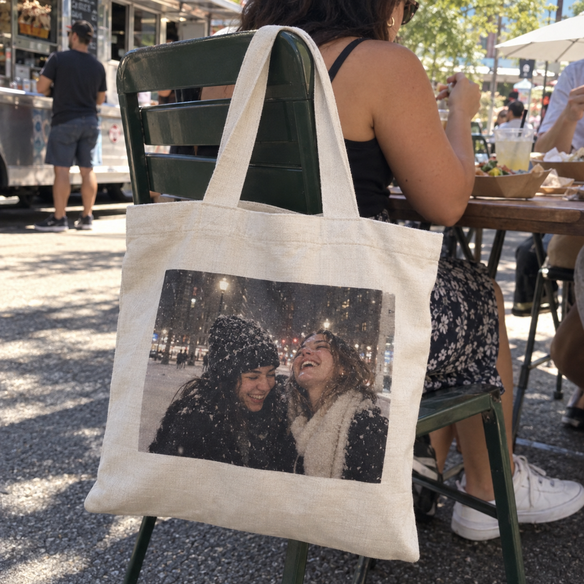 A fabric tote bag printed with a snowy photo of friends at a street food table.