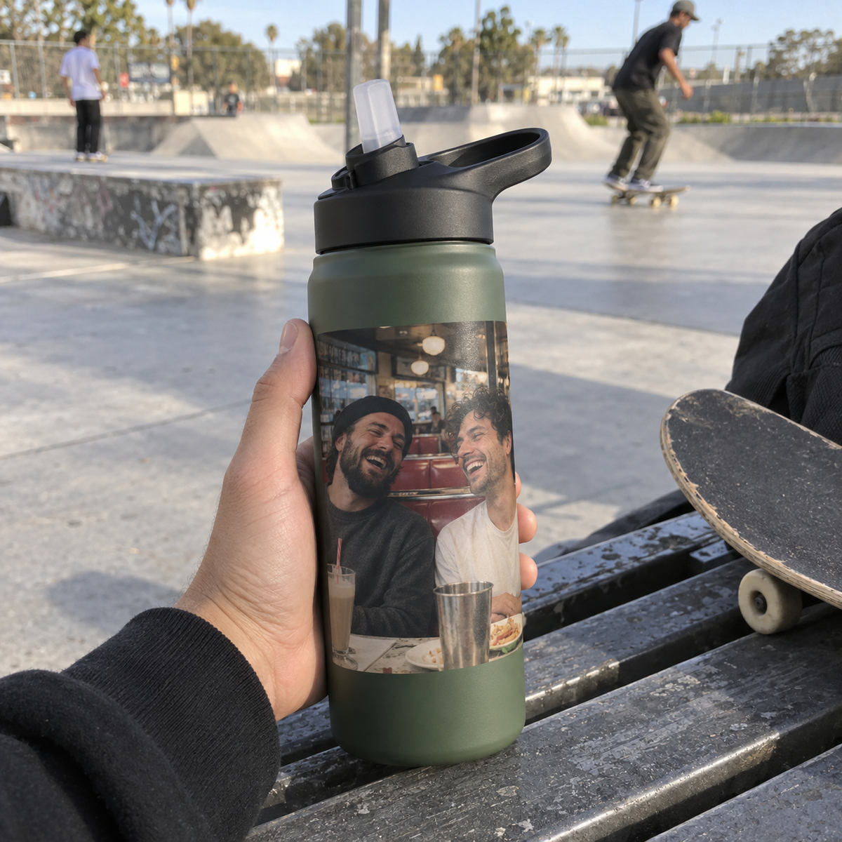 Sports bottle with a photo of two friends laughing at a café, held at a skate park.