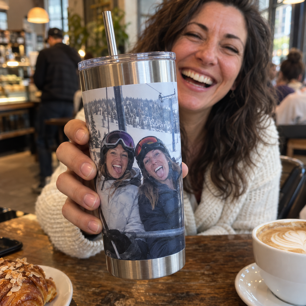 A vacuum tumbler printed with two sisters on a ski trip, held in a café.