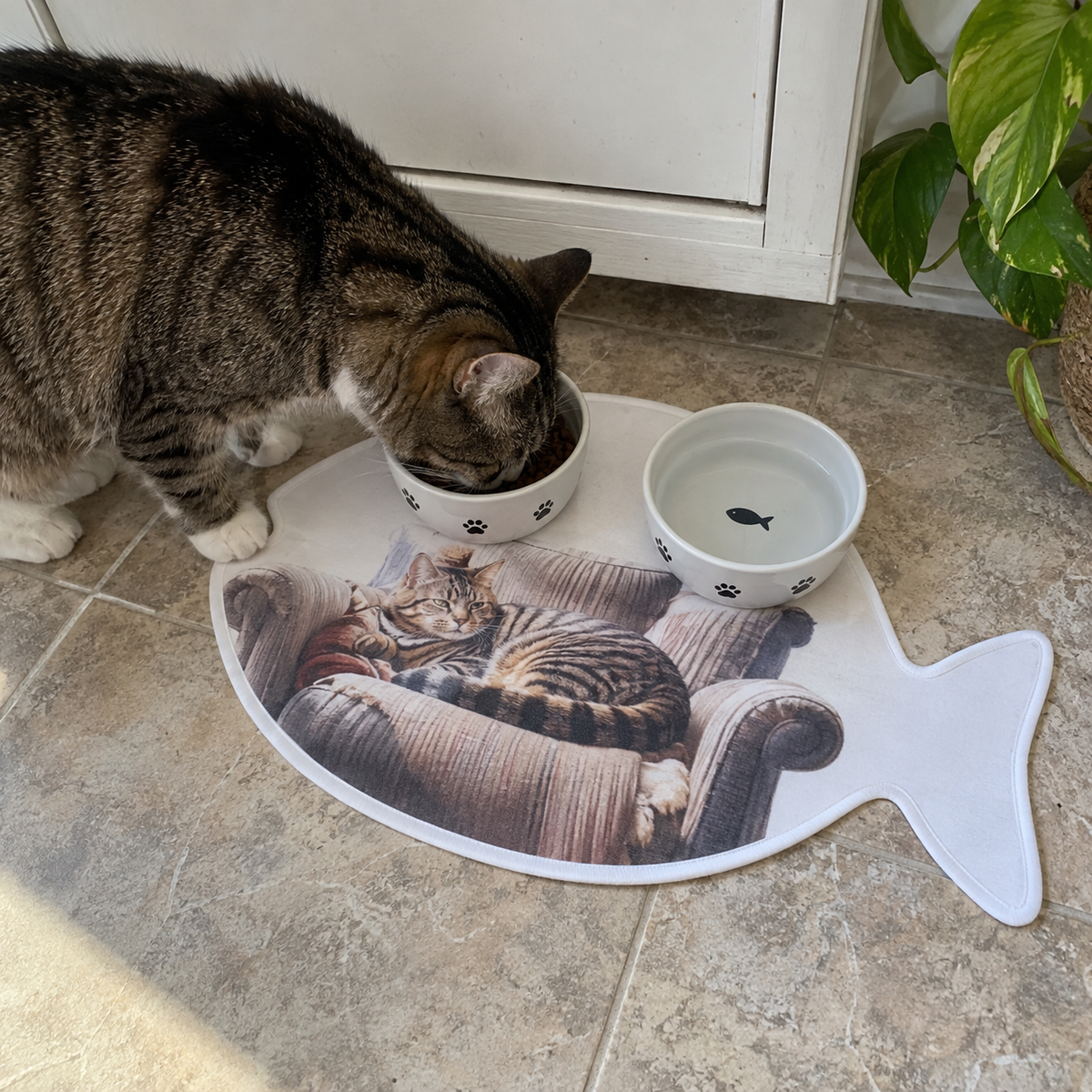 A fish-shaped feeding mat printed with a cat on a chair.