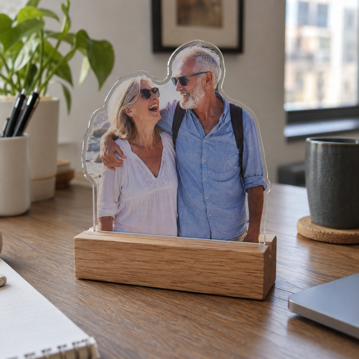 Unlit custom-shaped acrylic night light printed with an older couple's seaside photo on a desk.