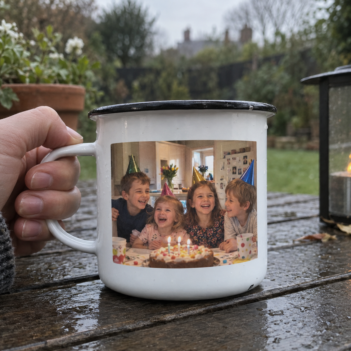 Enamel camping mug printed with an old family birthday photo on a rainy garden table.