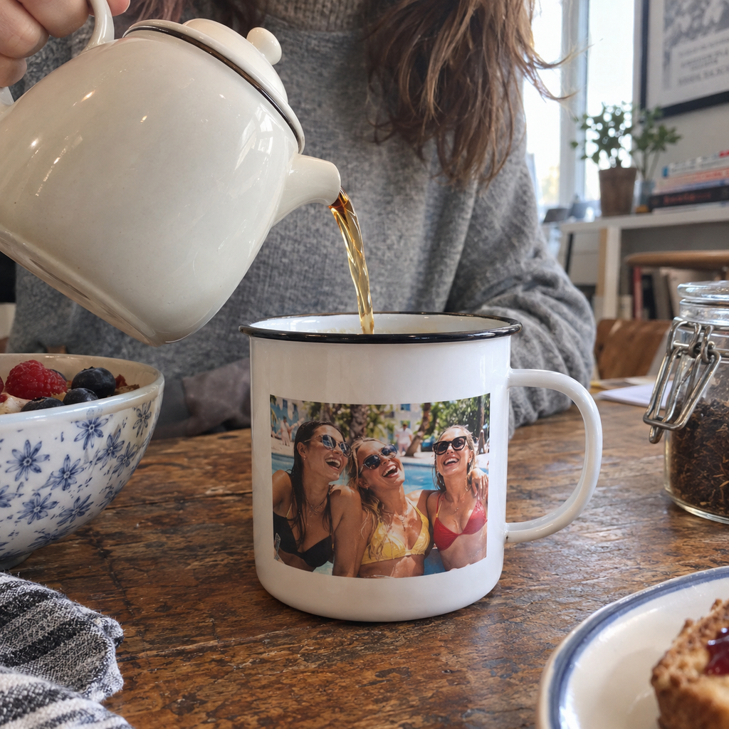 White enamel camping mug printed with a summer pool party photo, photographed at an indoor breakfast table.